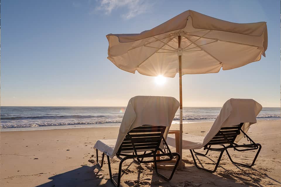 Beach lounge chairs with white umbrella and ocean view at sunrise or sunset
