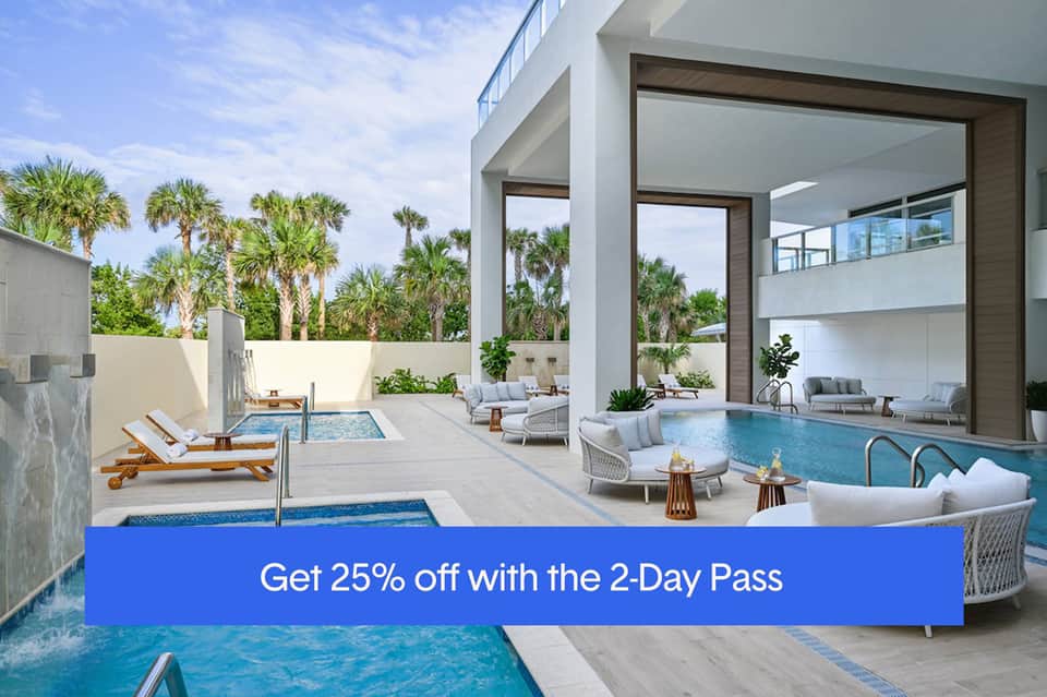 Modern resort courtyard with indoor-outdoor pool, white furnishings, palm trees, and architectural glass walls