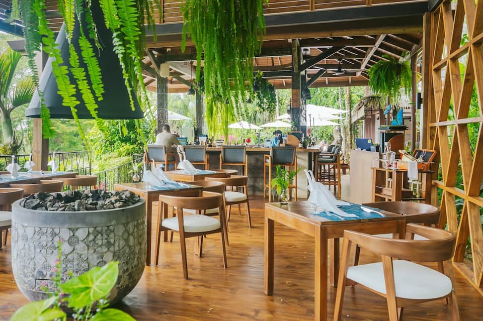 Lush restaurant terrace with hanging green plants, wooden furniture, fire pit, and open air design
