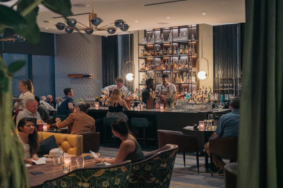 Modern hotel bar lounge with elegant black bar, liquor shelves, warm lighting, and seated guests