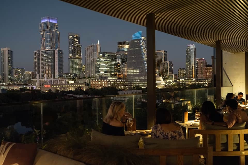 Upscale rooftop dining venue with floor-to-ceiling windows overlooking illuminated city skyline at dusk
