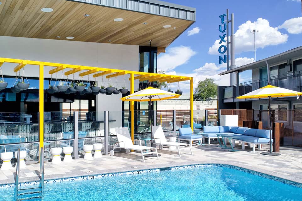 Contemporary pool deck with yellow pergola, modern furnishings, lounge chairs, and resort building