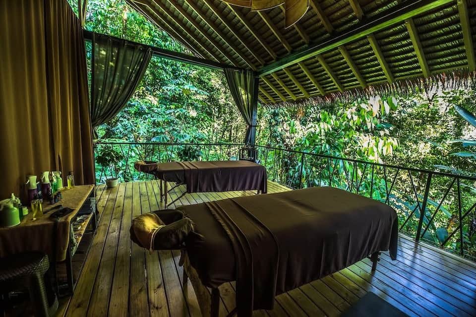 Luxury spa treatment bed on wooden deck overlooking lush green forest canopy