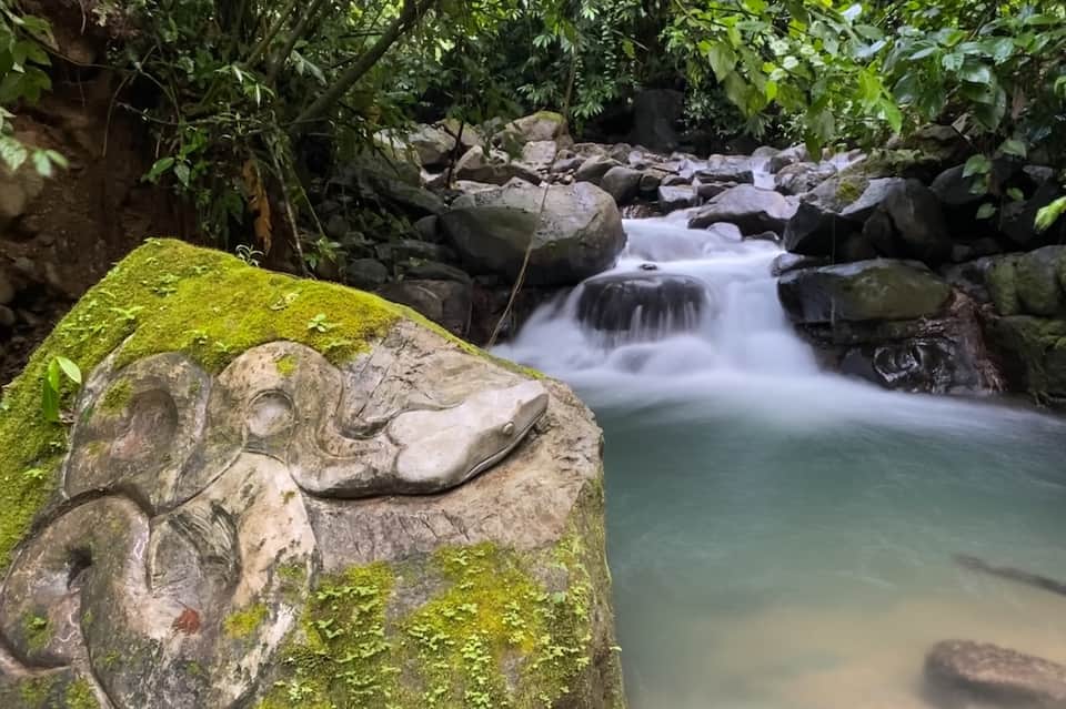 Moss-covered rock with carved design overlooking cascading stream and lush jungle vegetation