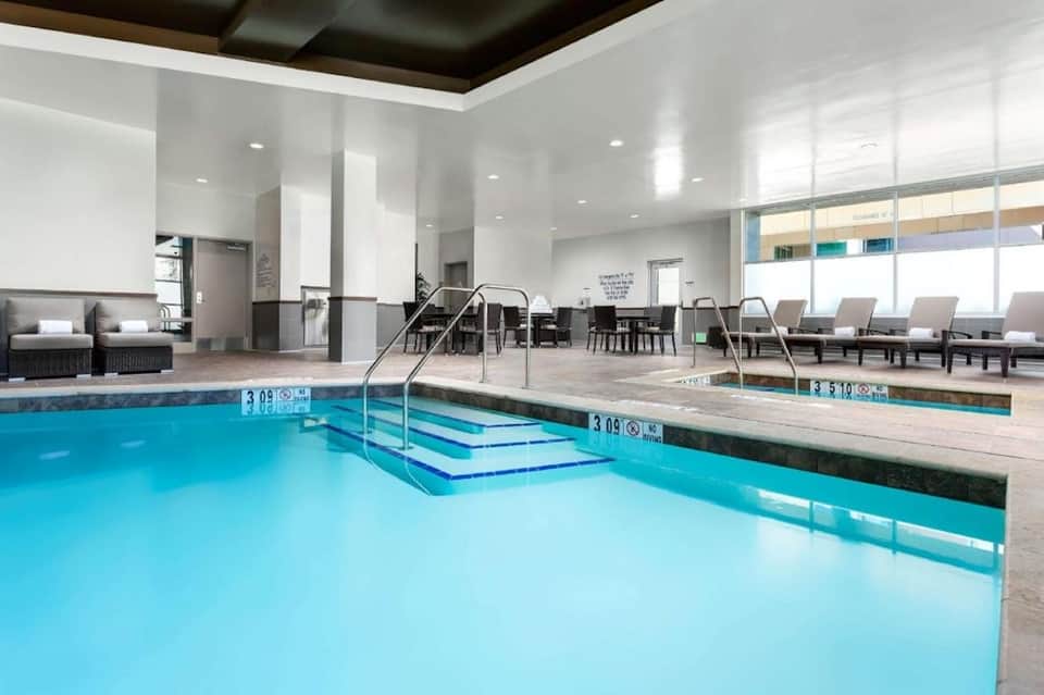 Indoor aquatic center with heated pool, spa, steps, seating area, and large windows