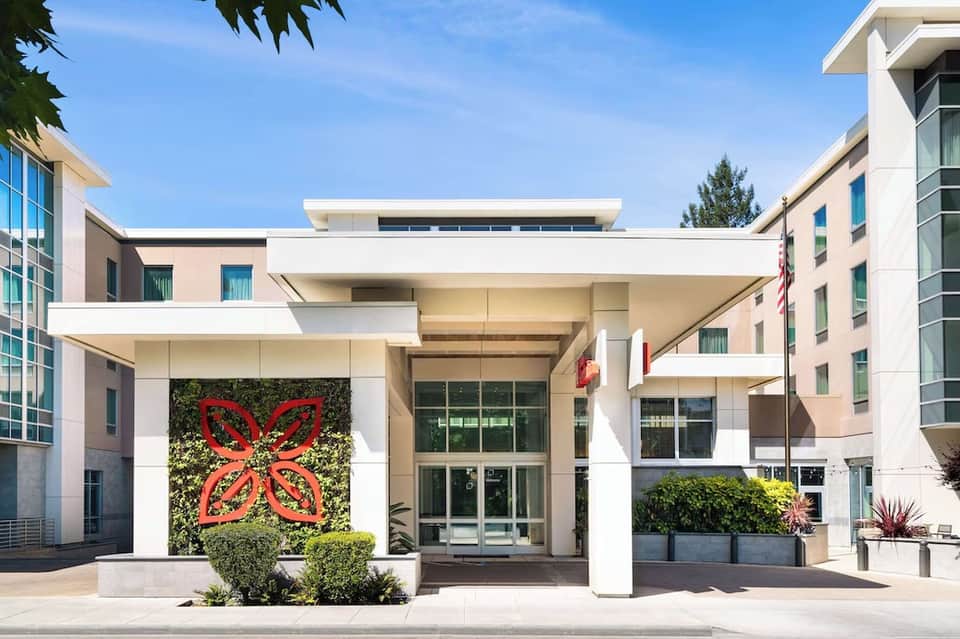 Modern hotel entrance with white architectural details, red art installation, and landscaping