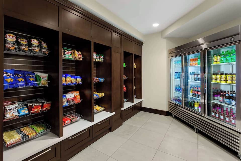 Hotel convenience store with dark wood snack shelves on left and refrigerated beverage cases on right