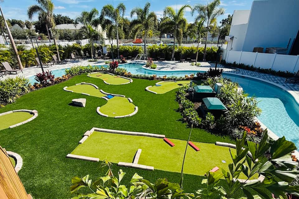 Miniature golf course with artificial turf, white bunkers, palm trees, and resort pools in background