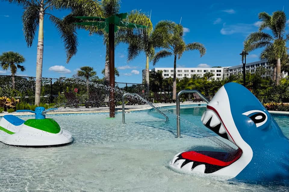 Shallow resort pool with colorful playful whale sculpture and palm trees in tropical setting