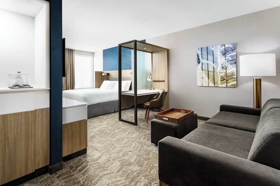 Modern hotel suite with four-poster bed, sitting area, wood accents, and contemporary design
