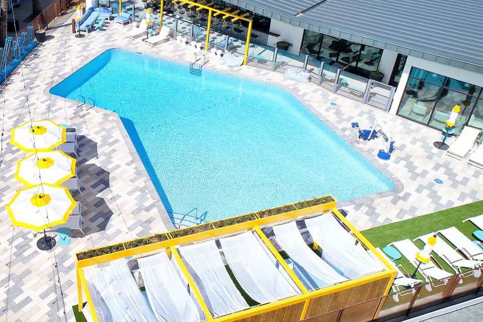 Large rectangular pool with bright blue water, yellow umbrellas, lounge chairs, and modern building facilities