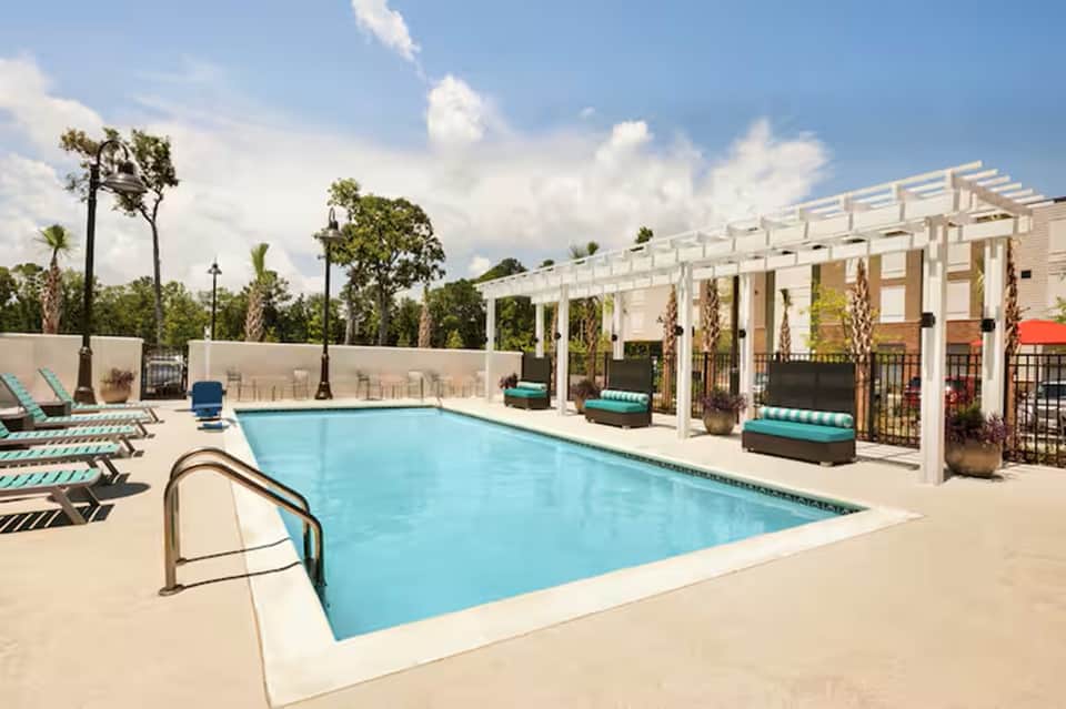 Resort swimming pool with white pergola shade structures and palm tree landscaping