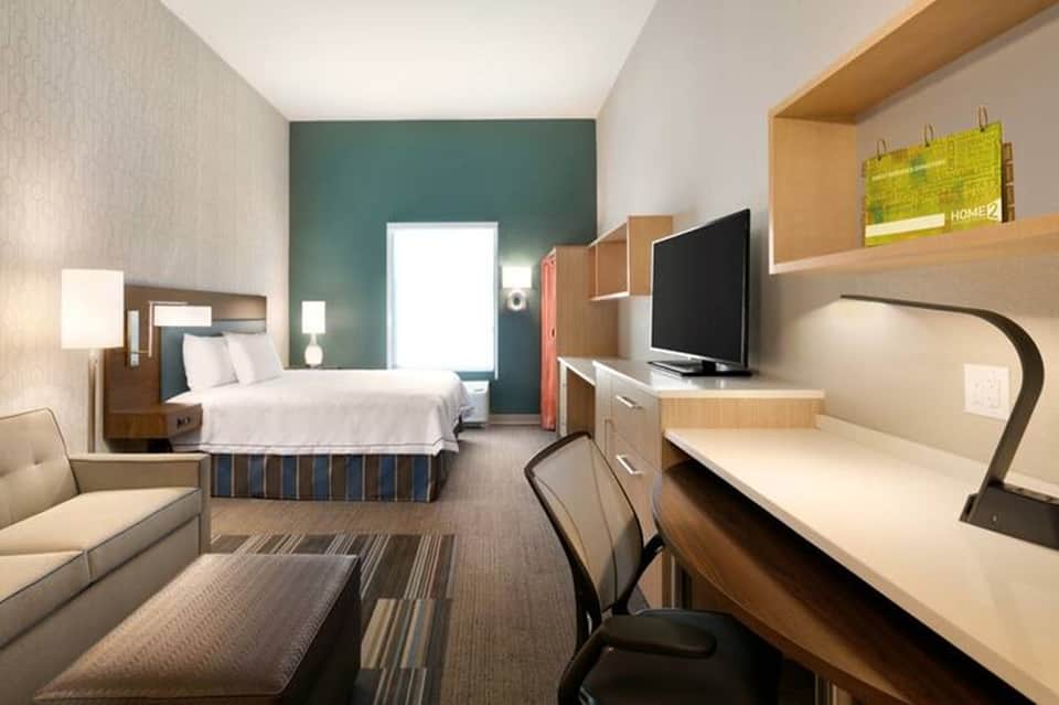 Modern hotel guest room with queen bed, desk, TV and teal accent wall
