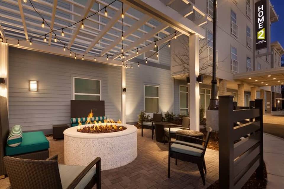 Modern outdoor fire pit lounge area at night with string lights, pergola, fireplace, and contemporary seating