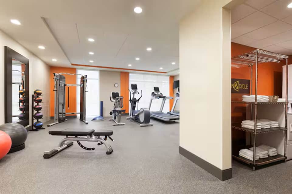 Hotel fitness center with orange accent walls, exercise equipment, and towel storage shelving