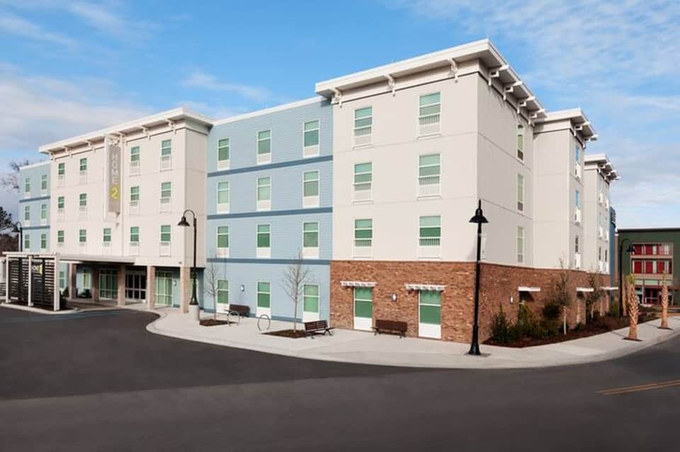 Modern four-story hotel building with light green and white facade and brick ground level