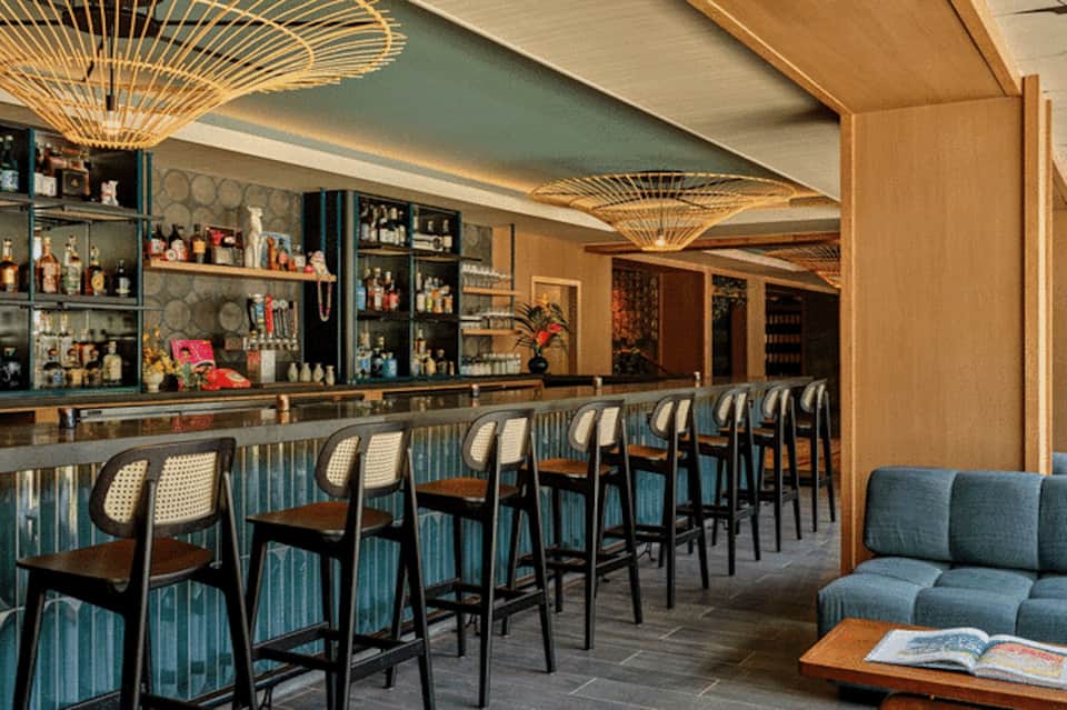 Upscale hotel bar interior with decorative ceiling fixtures, shelved liquor display, and blue-striped seating