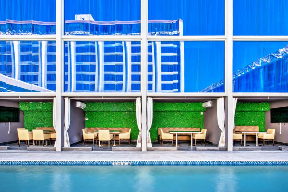 Resort poolside with blue cabanas, green living walls, yellow lounge chairs, and modern white pergola structures