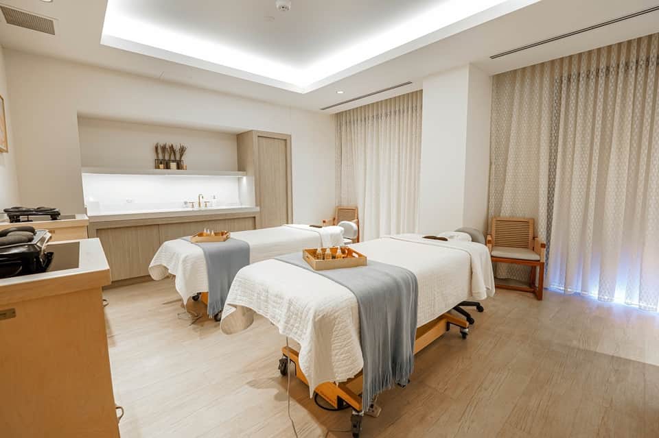 Spa treatment room with two massage tables, neutral décor, ambient lighting, and modern minimalist design