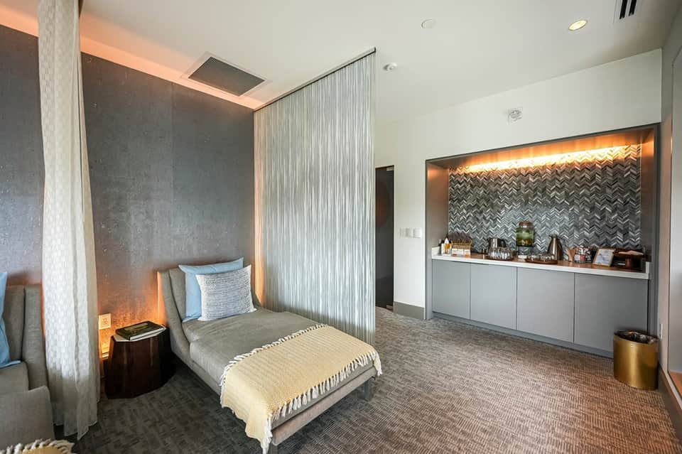 Modern spa treatment room with massage bed, herringbone tile backdrop, and ambient lighting
