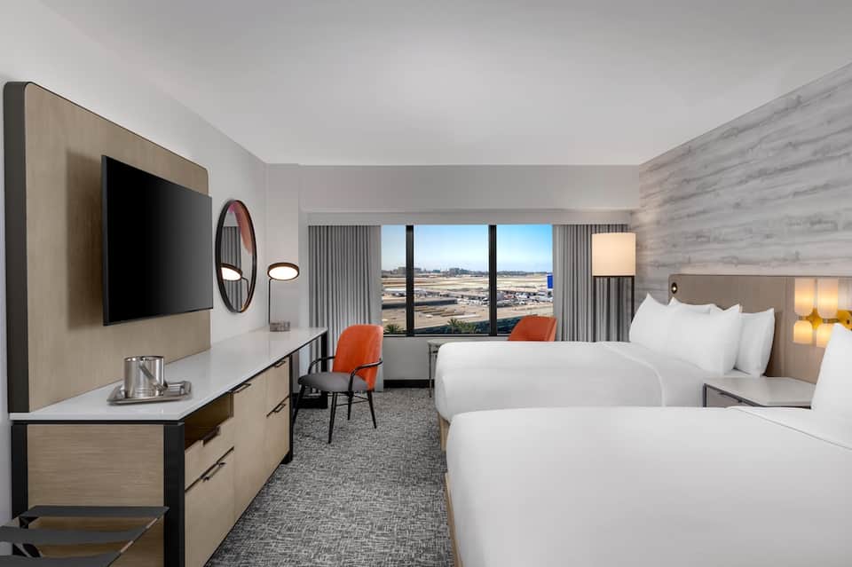 Modern hotel room with two queen beds, city view windows, and contemporary furnishings