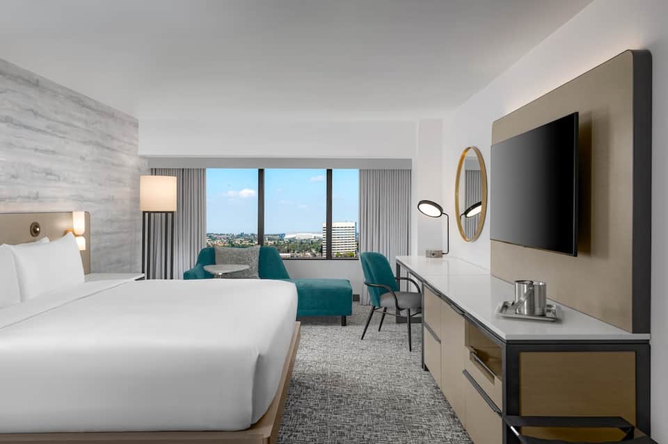 Modern hotel room with king bed, teal seating, and city skyline view