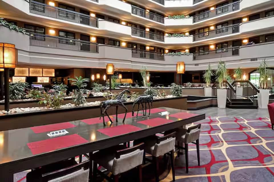 Multi-level hotel atrium with pink carpeting, modern railings, plants, and distinctive architectural design