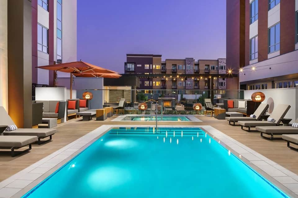 Urban rooftop pool at twilight surrounded by modern buildings with lounge seating