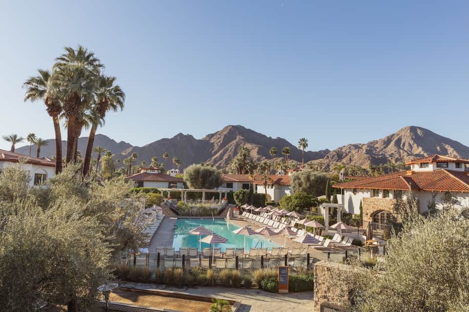 Desert resort pool area surrounded by palm trees with mountains and Spanish colonial architecture