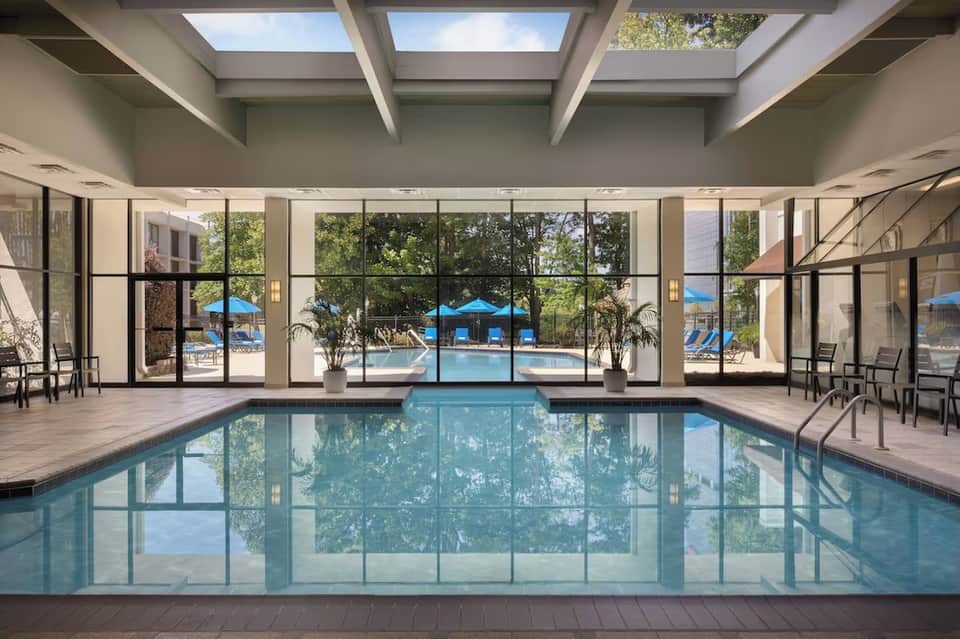 Indoor swimming pool with floor-to-ceiling windows overlooking outdoor pool and grounds