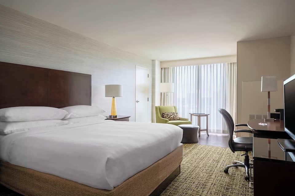 Contemporary hotel room with queen bed, green accent chair, and balcony access