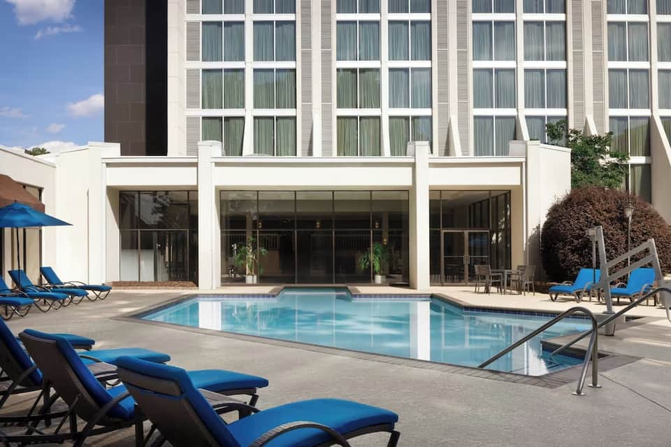 Hotel courtyard pool with rectangular design, blue lounge chairs, modern white facade building with grid windows, and manicured landscaping