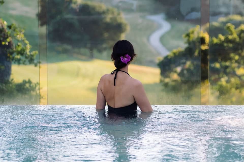 Woman in an infinity pool overlooking rolling green countryside landscape