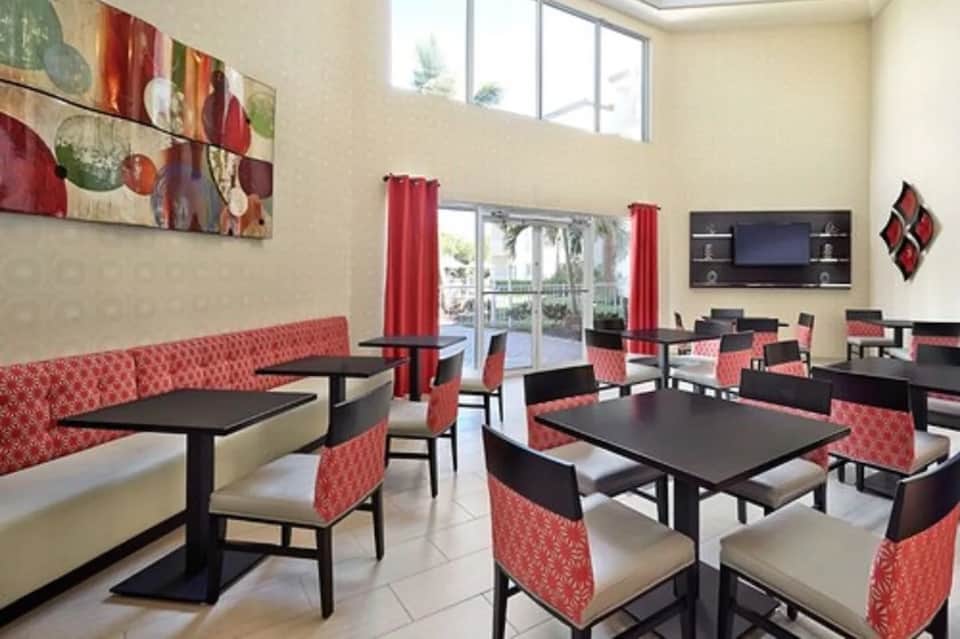 Hotel lounge with red patterned seating, black tables, palm views, and modern décor