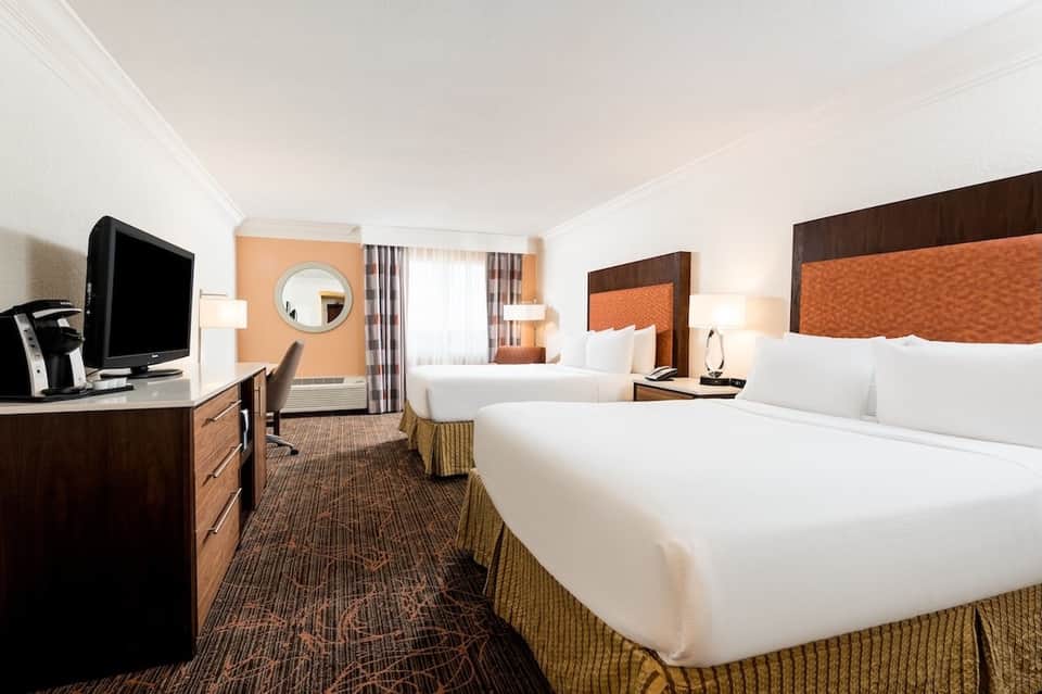 Hotel room with two double beds, wood headboards, desk, and warm lighting