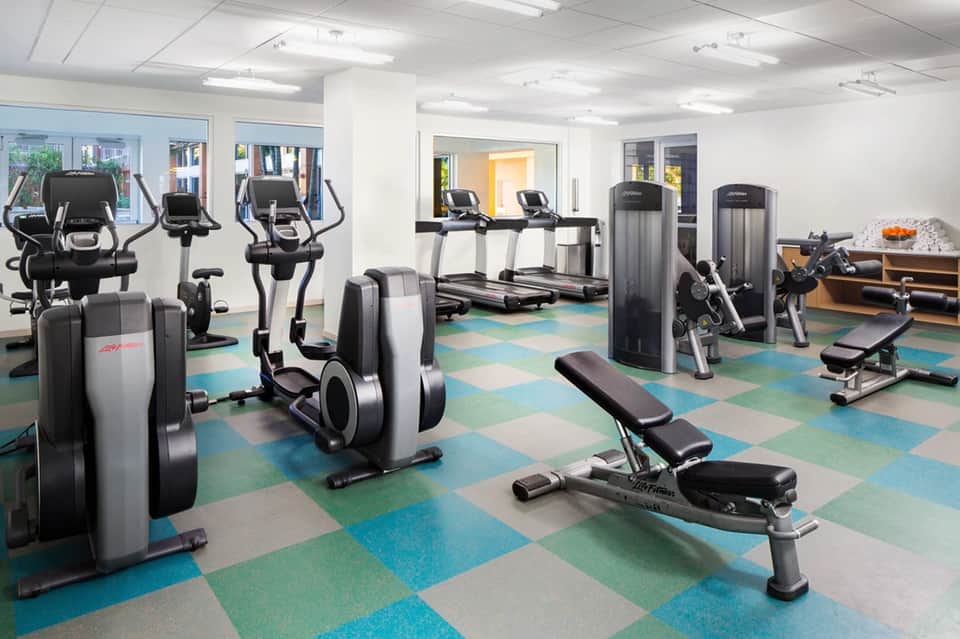Bright fitness center with cardio equipment, treadmills, stationary bikes, and colorful diamond-pattern flooring