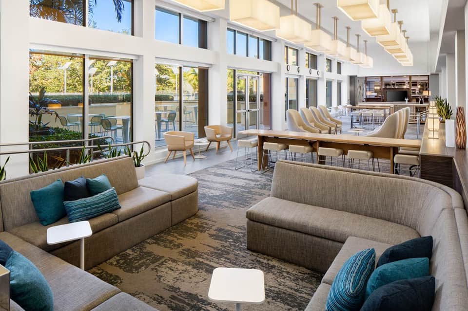 Bright modern resort lounge with neutral sofas, floor-to-ceiling windows, outdoor deck, fireplace, and contemporary furnishings