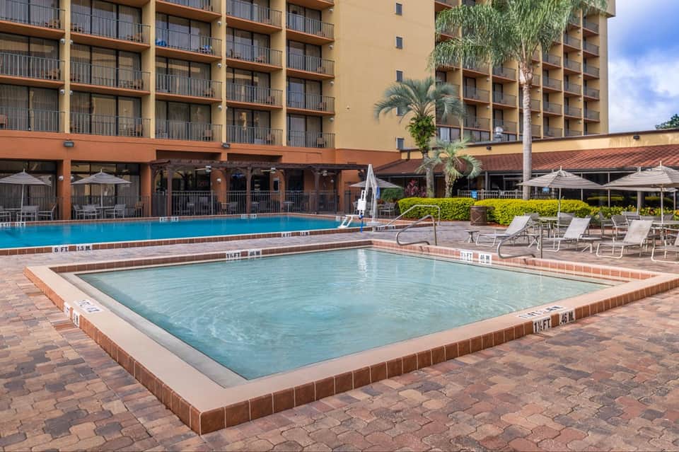 Multi-story hotel with ground-level pool, lounge seating, palm tree, and brick patio