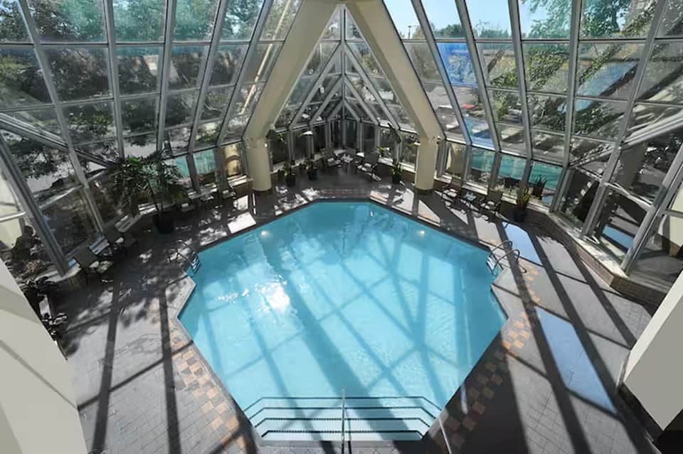 Glass-enclosed indoor pool with geometric ceiling beams and waterside seating