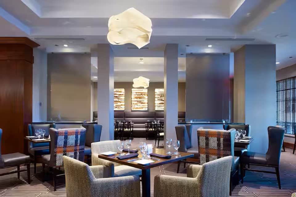 Upscale restaurant interior with cloud-shaped ceiling fixtures, blue accent chairs, neutral tones, and modern elegant design