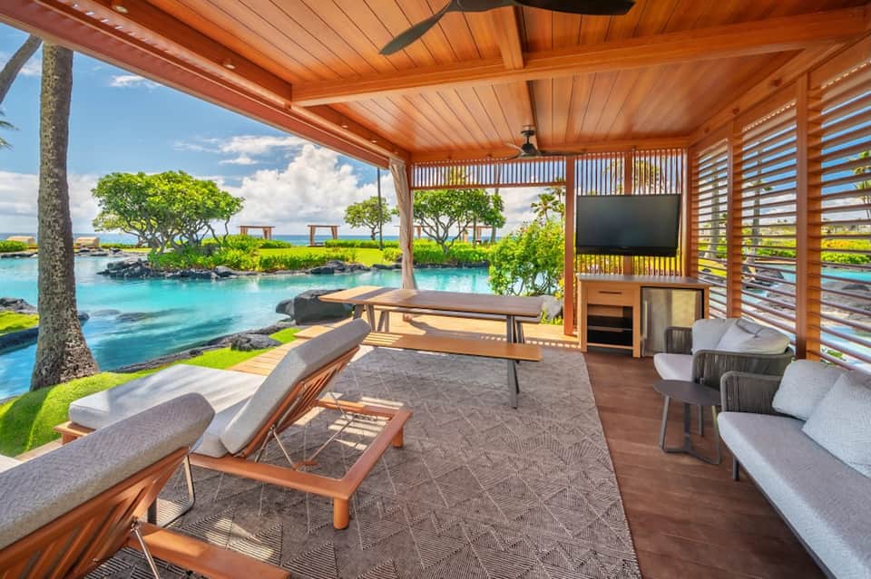 Oceanfront cabana with wooden architecture, lounge seating, TV, and stunning water views