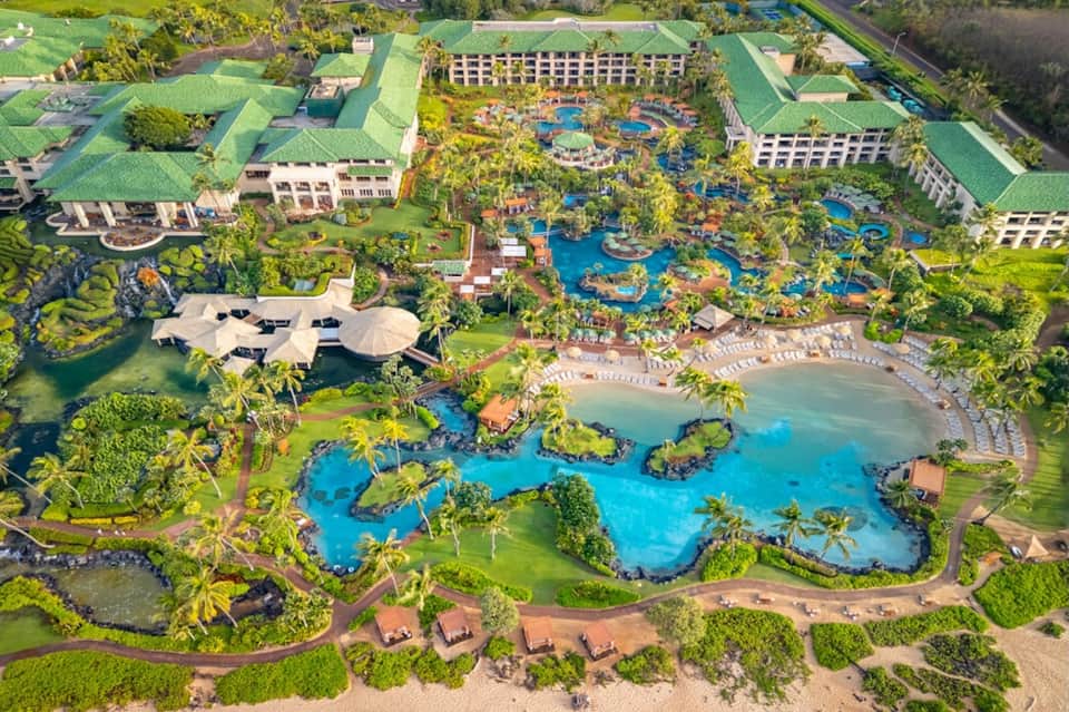 Aerial resort view with multiple blue pools, palm trees, beach, and hotel buildings