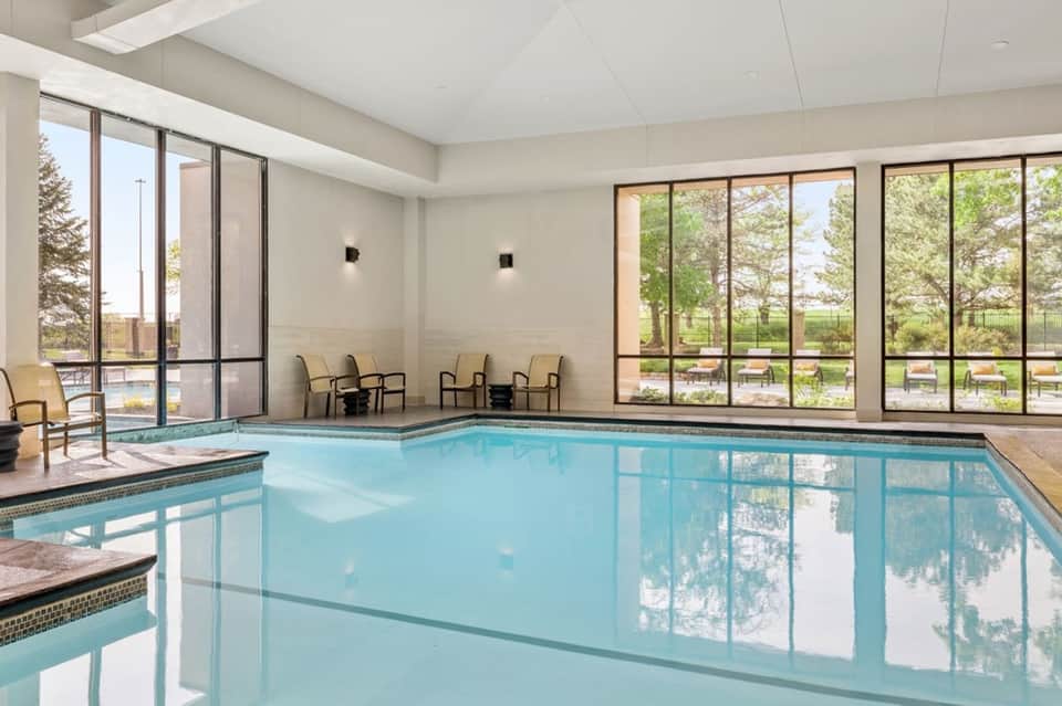 Indoor heated pool with large windows overlooking landscaped grounds and outdoor seating
