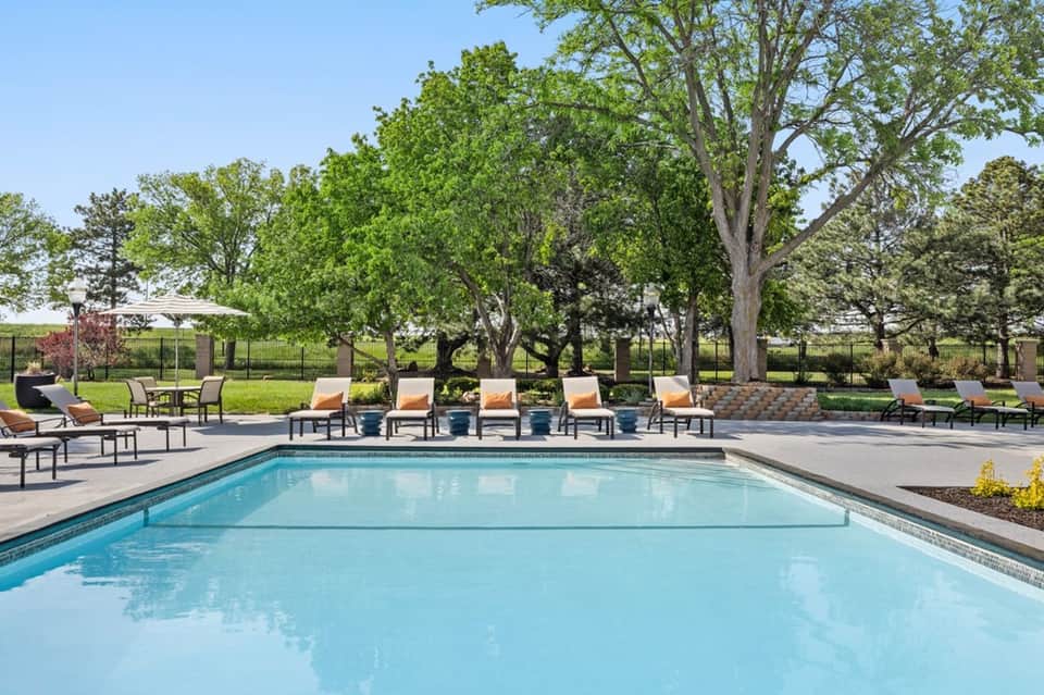 Pristine rectangular pool surrounded by loungers with orange cushions beneath mature shade trees