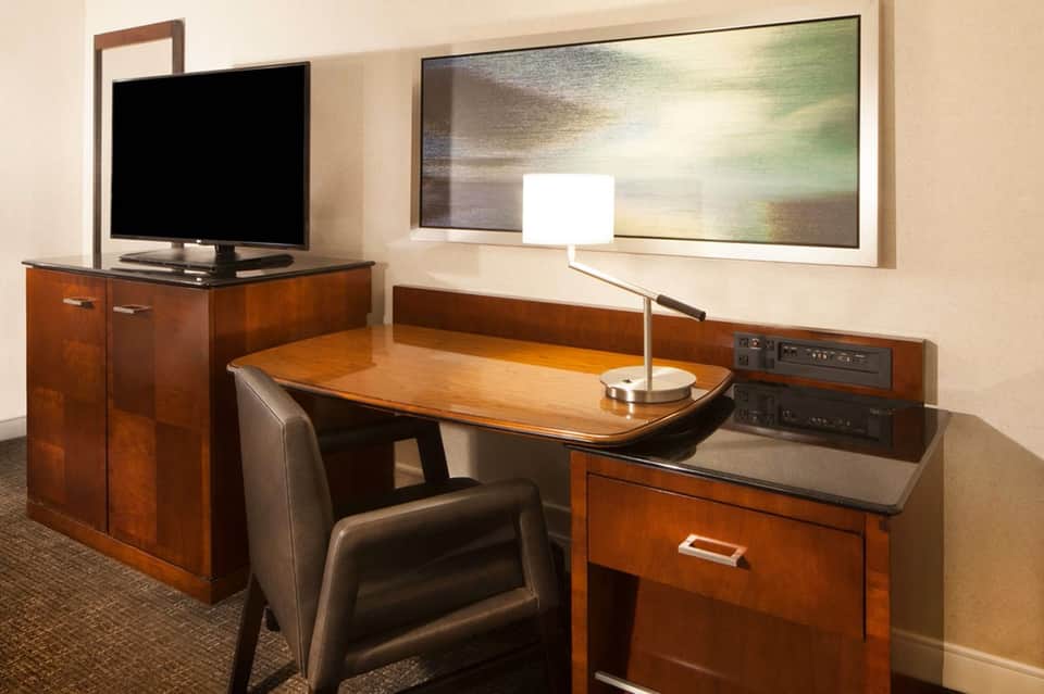 Hotel room workspace with wooden desk, leather chair, TV, mirror, and desk lamp