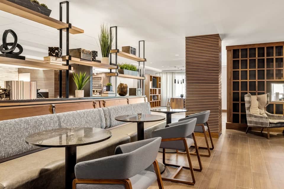 Modern café or lounge with gray seating, wooden shelving, plants, and contemporary interior design