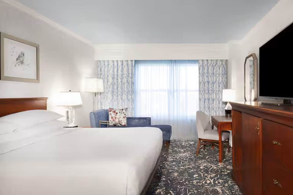 Bright hotel room with two queen beds, blue patterned curtains, and seating area with ocean view doors