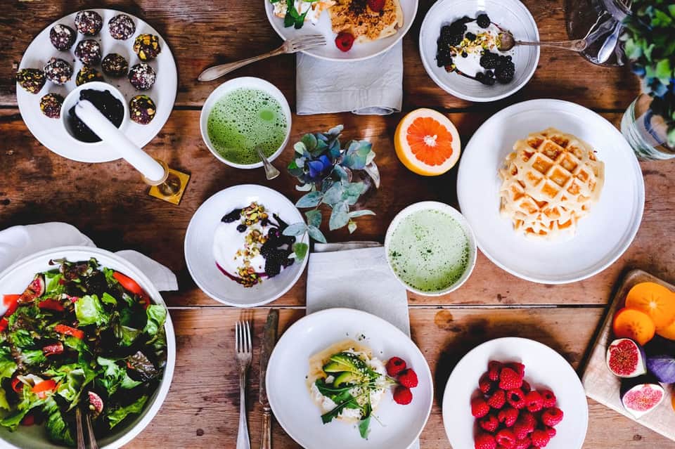Overhead view of colorful breakfast spread with waffles, salads, smoothies, berries, and gourmet dishes on wooden table