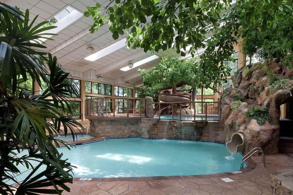 Indoor tropical pool with turquoise water, waterslide, lush plants, and rock features