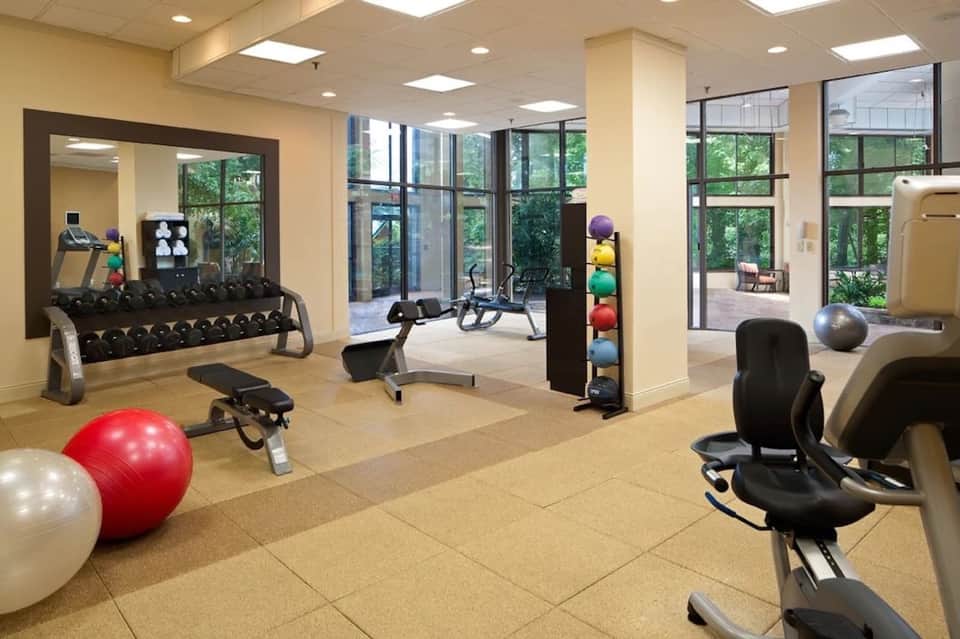 Fitness center with exercise equipment, dumbbells, exercise balls, and large windows overlooking grounds